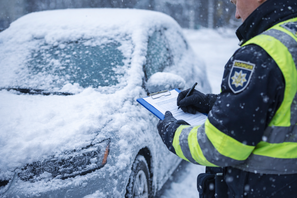 Поліцейський виписує штраф біля автомобіля, вкритого снігом, взимку