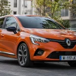Помаранчевий Renault Clio E-Tech Hybrid 2020 п’ятого покоління на міській вулиці, вигляд спереду та збоку.